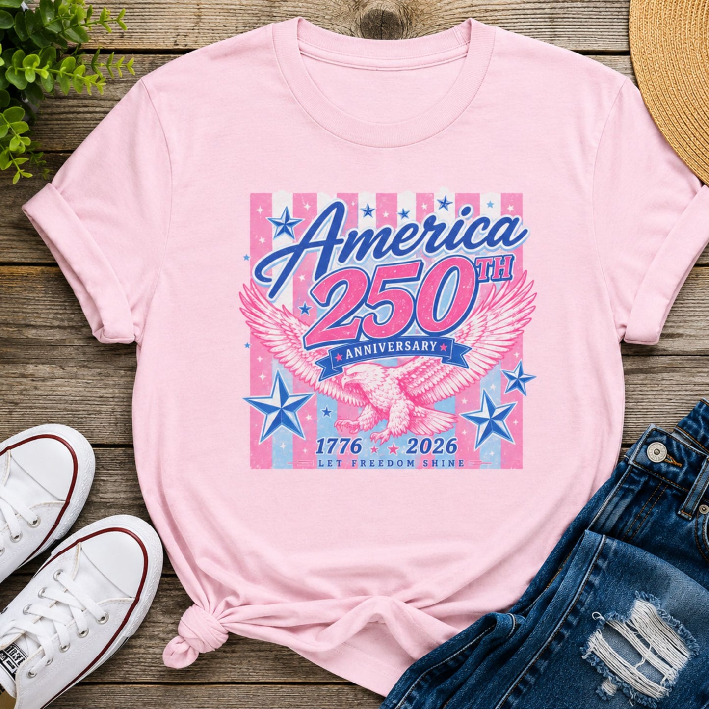 America 250th Anniversary patriotic graphic tee in light pink featuring a vintage eagle, stars, and 1776-2026 anniversary design styled with denim shorts and white sneakers.