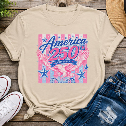 America 250th Anniversary eagle graphic t-shirt in sand color featuring pink and blue patriotic artwork styled with denim shorts and casual summer accessories.
