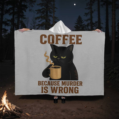Person holding a blanket with a black cat and coffee cup design in a forest setting.