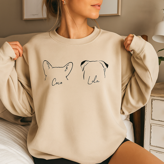 Personalized sand-colored dog sweatshirt featuring custom ear outlines and pet names “Coco” and “Lola,” cozy flat lay with jeans and greenery.