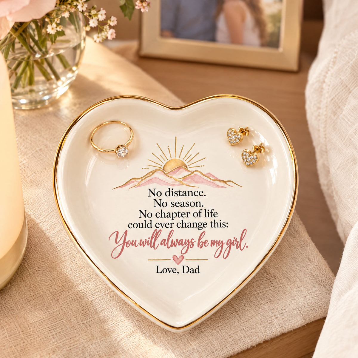 Heart-shaped daughter keepsake jewelry dish from Dad holding two gold rings on a warm cream vanity.